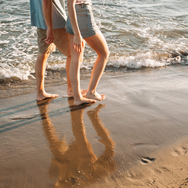 Una coppia passeggia a piedi scalzi sul bagnasciuga lungo il litorale di Caorle
